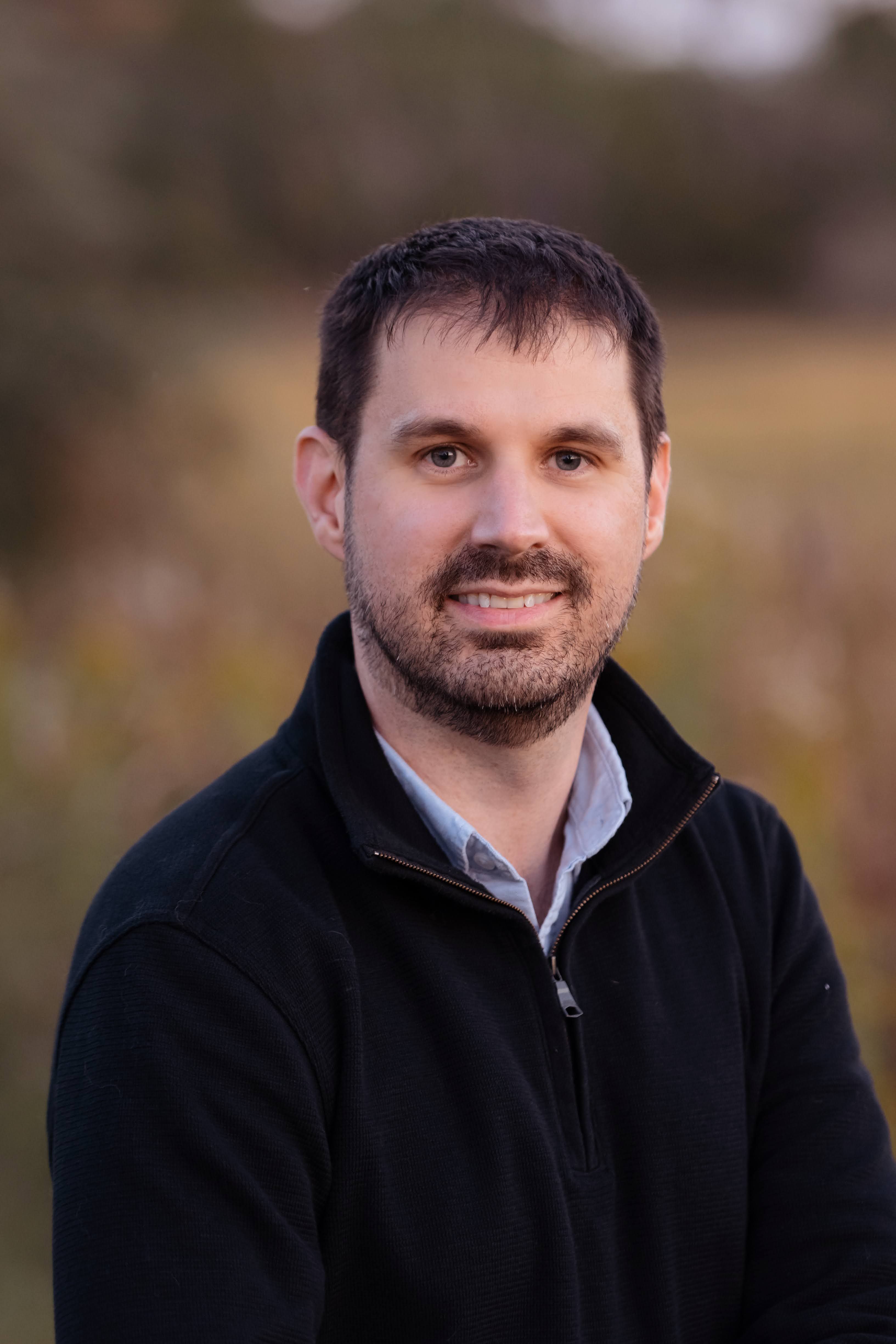 Brian Still, MD, smiling, in a dark quarter-zip sweater outdoors